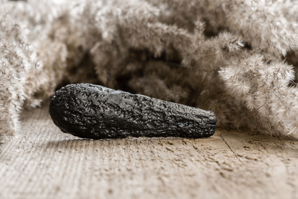 テクタイトのイメージ写真です / Raw tekctite stone on wooden background. Tektite crystal is a natural glass formed from terrestrial debris when an asteroid strikes the Earth